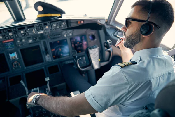Stralende man in uniform zittend op de stoel in de cockpit van het passagiersvliegtuig — Stockfoto