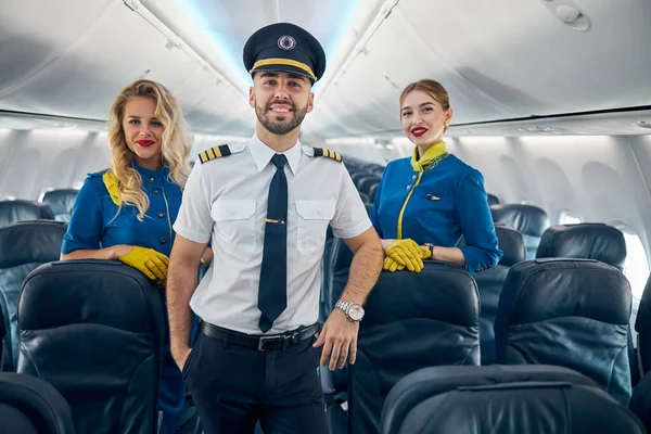 Boldog mosolygós jóképű pilóta két légi hostess a fedélzeten a repülőgép — Stock Fotó
