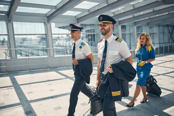 Pilotos alegres y azafata caminando por la terminal del aeropuerto — Foto de Stock