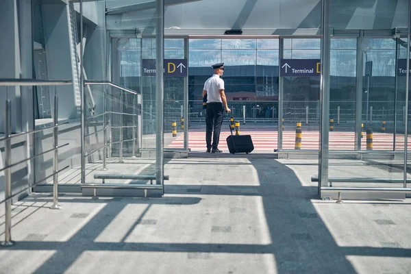 Piloto masculino com mala de viagem em pé fora do terminal do aeroporto — Fotografia de Stock