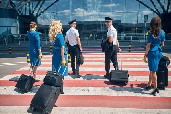 Pracownicy linii lotniczych z walizkami podróżnymi przejeżdżającymi przez ulicę na lotnisku — Zdjęcie stockowe