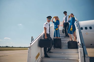 Güzel bayan hostesler ve iki yakışıklı pilot dışarıdaki fotoğraf makinesine bakıp poz veriyorlar.