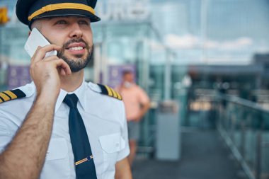 Havaalanında cep telefonuyla konuşan neşeli erkek pilot.