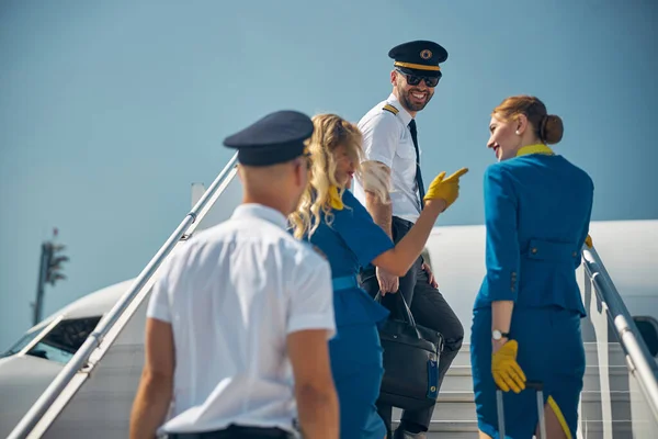 Belos comissários de bordo com colegas perto de rampa em movimento no aeroporto — Fotografia de Stock