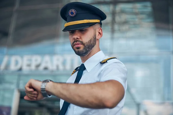 Handsome male pilot looking at wristwatch on the street — Stock Photo, Image