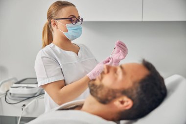 Adam yatağında yatarken elinde şırınga tutan bir güzellik uzmanı.