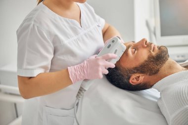 Yakışıklı genç adam lazer yüz tedavisi görüyor.