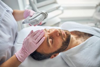 Yakışıklı genç adam kozmetik kliniğinde lazer yüz tedavisi görüyor.