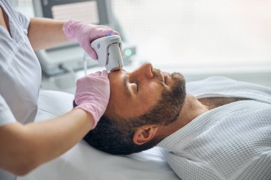 Doktor kozmetik uzmanı erkek derisini lazer cihazıyla tedavi ediyor.