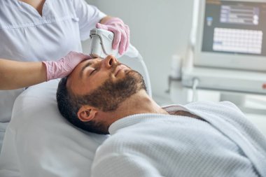 Doktor güzellik uzmanı erkek tenini lazer cihazıyla tedavi ediyor.