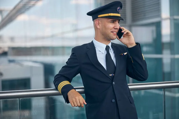 Vrolijke mannelijke piloot aan het praten op mobiele telefoon op de luchthaven — Stockfoto