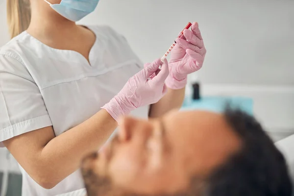 Doutor cosmetologista segurando seringa enquanto o homem deitado no leito do dia — Fotografia de Stock