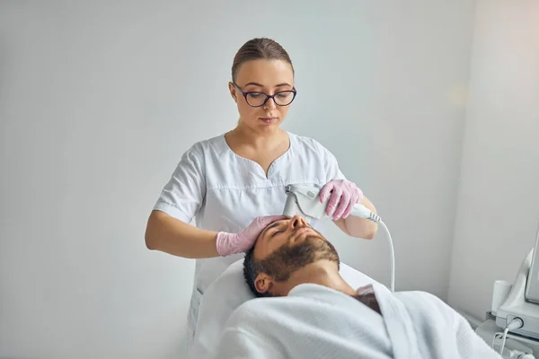 男性の皮膚をレーザー装置で治療する女性美容師 — ストック写真