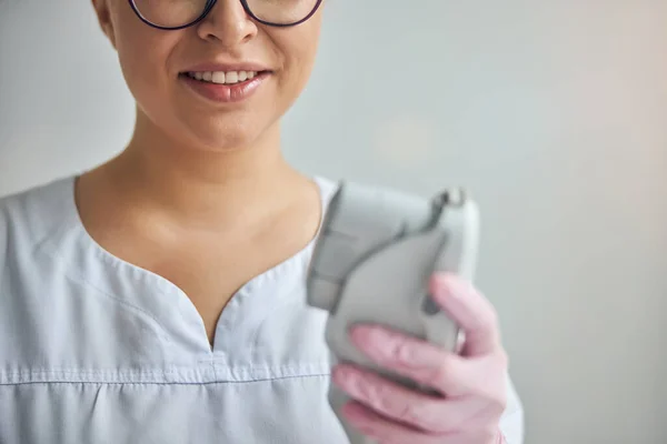 Cosmetologista sorridente fêmea está segurando dispositivo laser — Fotografia de Stock