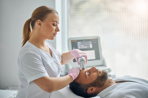 Charmante Kosmetikerin behandelt männliche Haut mit Lasergerät — Stockfoto