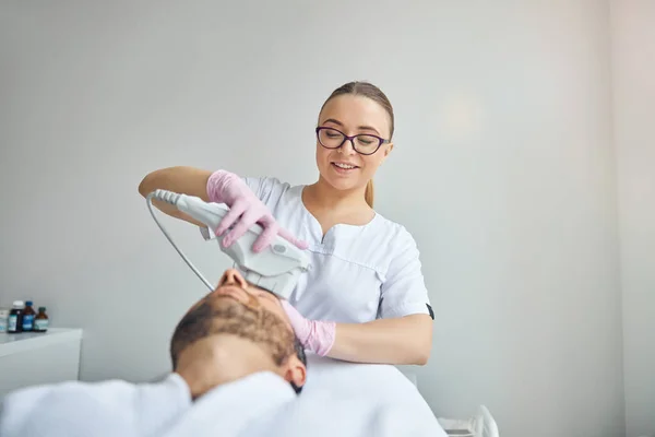 Cosmetologist alegre que trata a pele masculina com dispositivo do laser — Fotografia de Stock