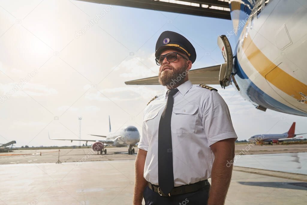 Confident pilot posing next to the plane in the airport