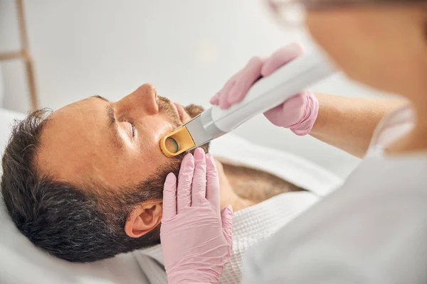 Esthetician removing unwanted hair from male cheek with laser device — Stock Photo, Image