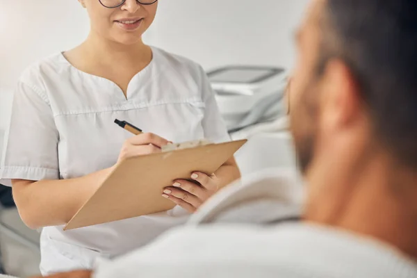 Esteticista feminina conversando com o jovem e tomando notas — Fotografia de Stock