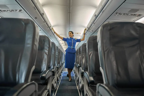 Успокаиваемая профессиональная стюардесса улыбается в салоне самолета — стоковое фото