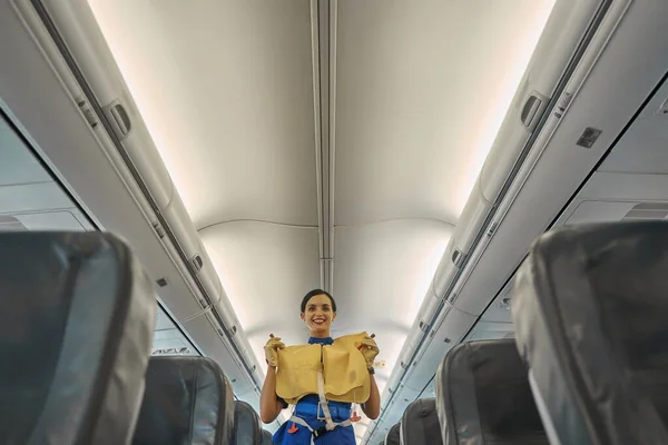 Pozitivní letuška demonstrující záchrannou vestu v kabině letadla — Stock fotografie