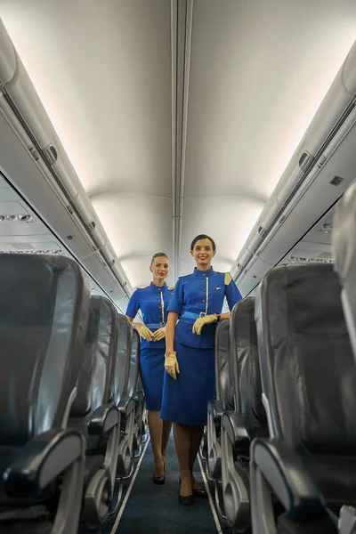 Two beautiful flight attendants standing between the seat rows — Stock Photo, Image