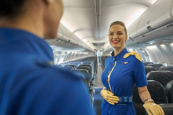 Veselá letuška se usmívá svému kolegovi v letadle — Stock fotografie