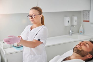 Neşeli güzellik uzmanı ameliyattan önce steril eldiven takıyor.