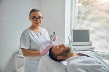 Yakışıklı genç adam kozmetoloji dolabında lazer yüz tedavisi görüyor.