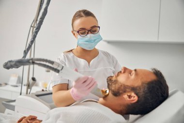 Tıraşsız genç adam lazer tüy çıkarma prosedüründen geçiyor.