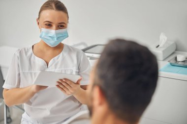 Tablet bilgisayarlı çekici bir estetisyen erkek hastayla konuşuyor.