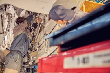 İki tamirci bir uçak hangarında açık bir jet parçasını inceliyor.