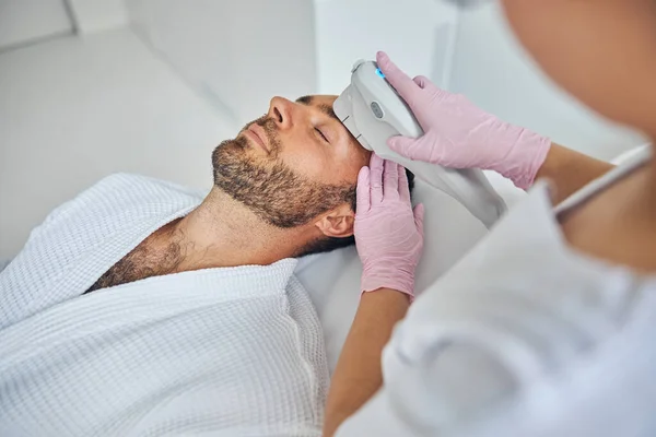 Esteticista em luvas estéreis tratando a pele masculina com dispositivo laser — Fotografia de Stock