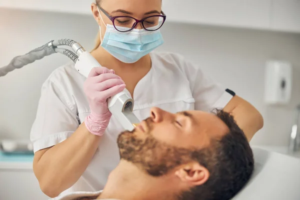Estetista in maschera medica che esegue la procedura di depilazione laser — Foto Stock