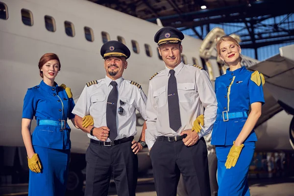Smiling and friendly professional pilot and air stewardesses standing in front of passenger airplane — Stock Photo, Image