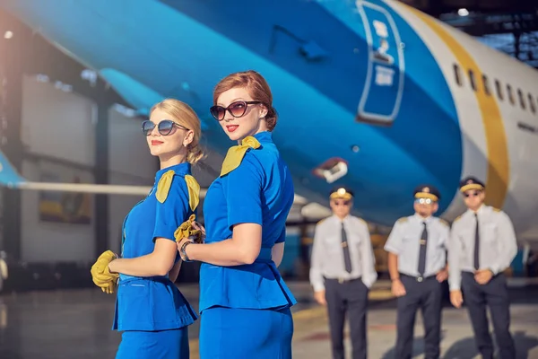 Elegantes azafatas femeninas en gafas de sol que caen felices mientras trabajan en el aeropuerto — Foto de Stock