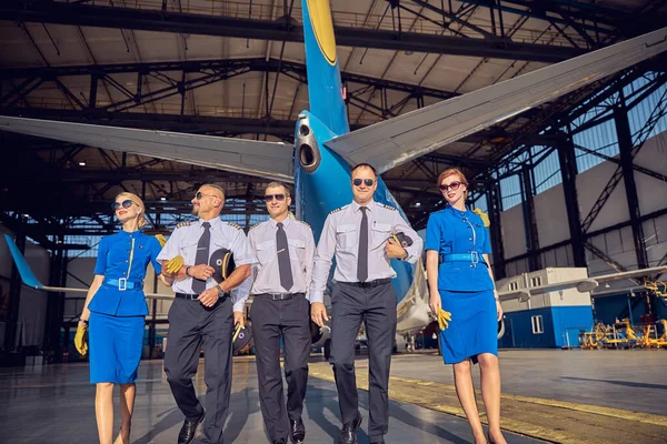 Três homens confiantes com duas anfitriãs de ar de mulher em uniforme elegante e óculos de sol — Fotografia de Stock