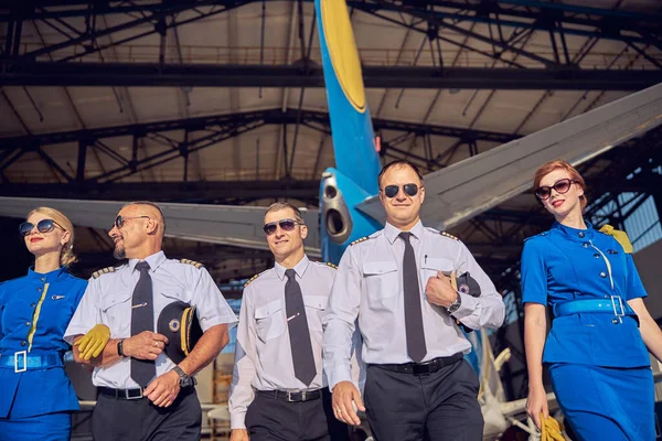 Maschi fiduciosi con belle femmine in uniforme aziendale trascorrere del tempo nel garage di aeroplano — Foto Stock