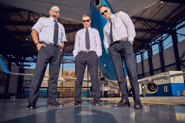 Beautiful stewardess with handsome men posing at the photo camera in front of big commercial airplane — Stock Photo, Image