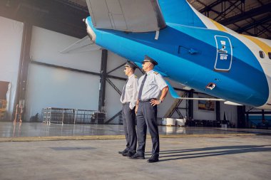 Pilot şapkalı yakışıklı beyaz adamlar güneşli bir günde açık havada yan tarafa bakarlar.