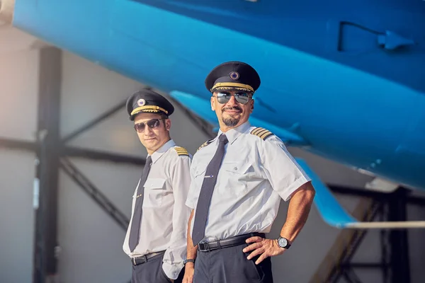 Happy smiling men in sunglasses standing in the hangar at the airport — Stock Photo, Image