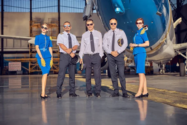 Feliz sorrindo três homens em chapéus ao ar livre perto da garagem de estacionamento do avião — Fotografia de Stock