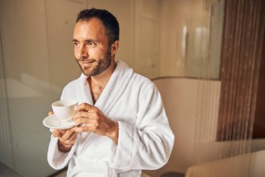 Neşeli genç adam spa salonunda kahve içiyor.