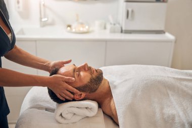Profesyonel masör elleri genç adamın yüzüne dokunuyor.