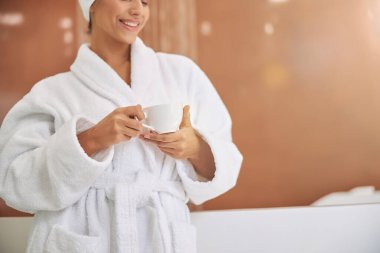 Bornozlu, elinde bir fincan kahveyle neşeli genç bir kadın.