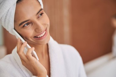 Duştan sonra cep telefonuyla konuşan neşeli genç bir kadın.