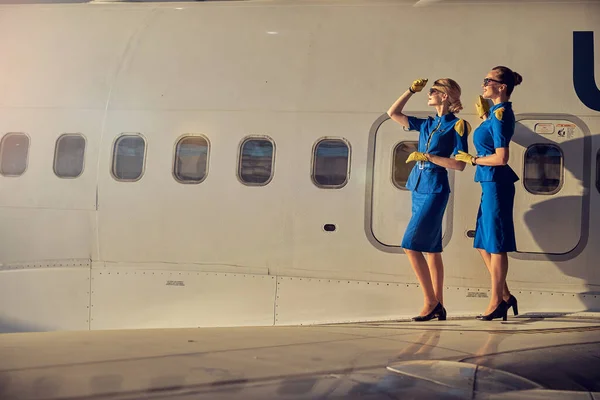 Две элегантные красивые стюардессы, изолированные на фюзеляже коммерческого самолета — стоковое фото
