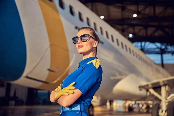 Elegante hospedeira aérea feminina cruzando os braços no hangar do aeroporto — Fotografia de Stock