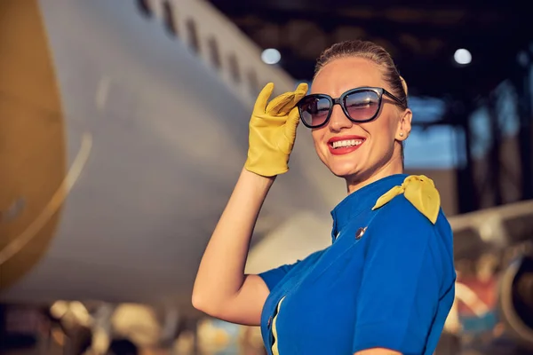 Очаровательная стюардесса в соответствующей форме и кожаных перчатках стоит на открытом воздухе в солнечный день — стоковое фото