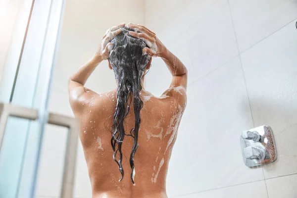 Bruna giovane donna che lava i suoi lunghi capelli sotto la doccia — Foto Stock